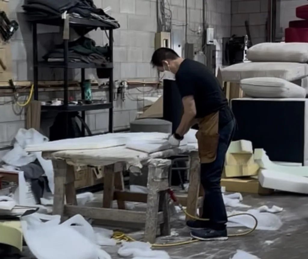 An Elite upholsterer cutting foam at the workbench, with fabric bolts and cushion stock stacked around the workshop