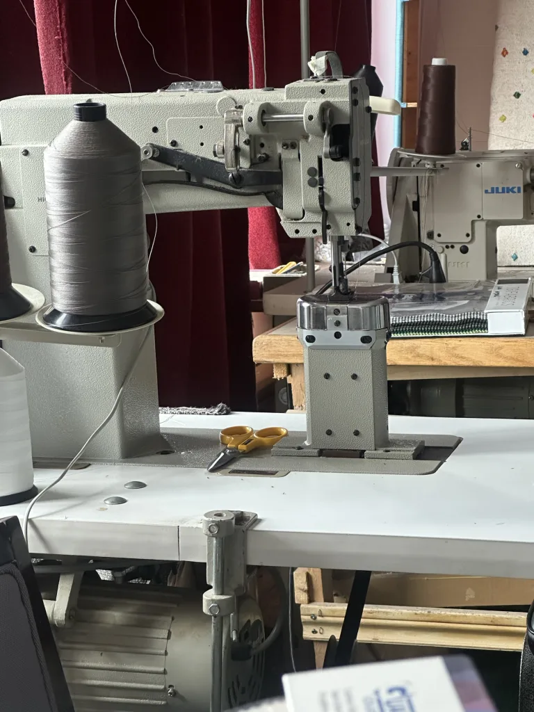 An industrial walking-foot sewing machine on the bench in Elite’s workshop, with cones of upholstery thread and shears beside it