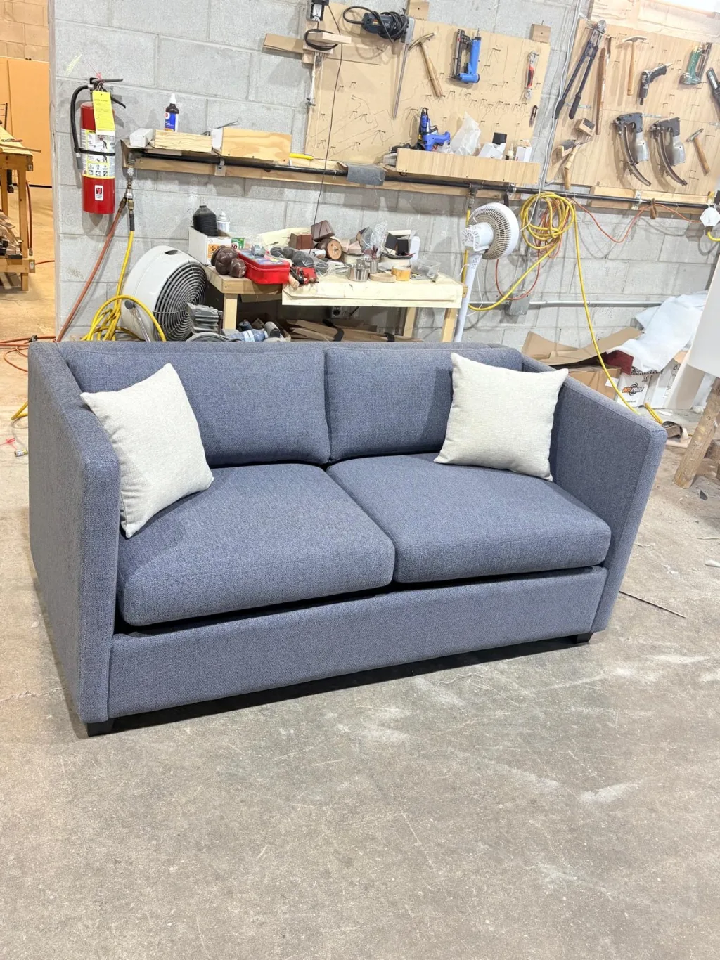 A blue-grey two-seat sofa with cream cushions, closed, in the Elite workshop