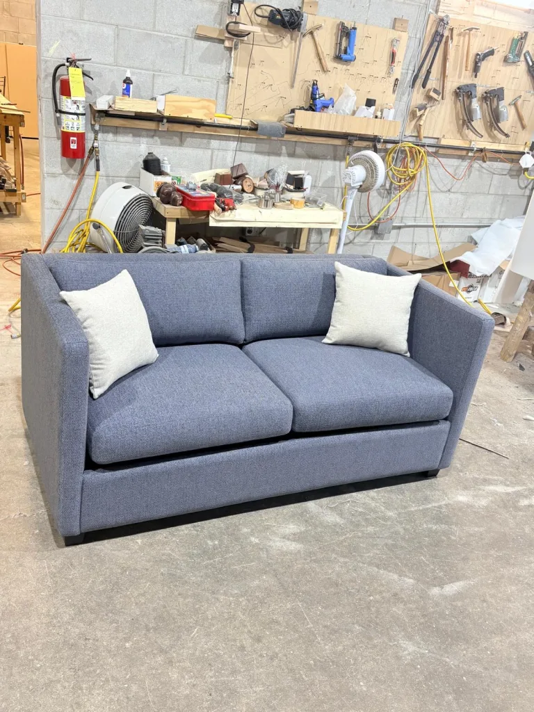 A blue-grey two-seat sofa with cream cushions, closed, in the Elite workshop