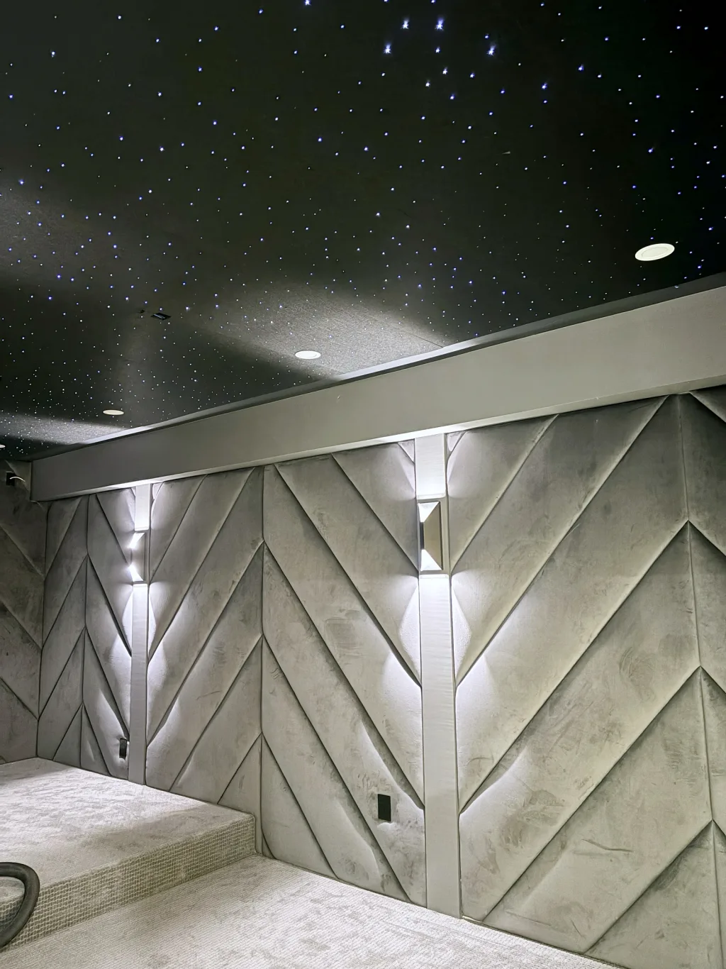 The chevron acoustic panelling in close-up, washed by narrow sconces, with the fibre-optic star ceiling above it