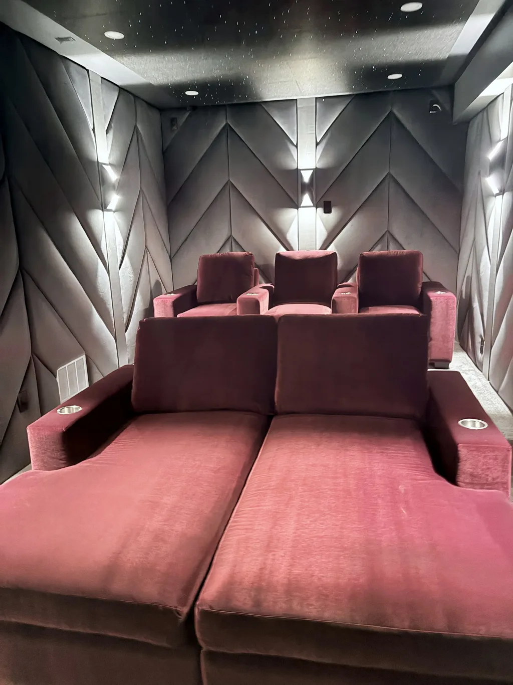 The theatre room straight down its centre line, both rows of red velvet seating between two facing walls of chevron panelling