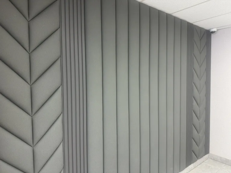 A wall of sage upholstered panelling running floor to ceiling, chevron sections meeting plain vertical channels and a narrow slatted band