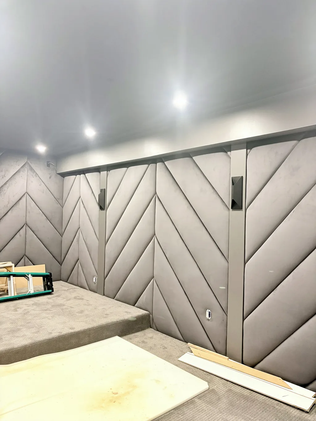 A long run of grey chevron panelling fitted along a wall, with the seating riser built but not yet carpeted